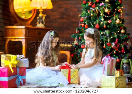 girls in beautiful dresses are sitting on the floor near the Christmas tree, open gifts