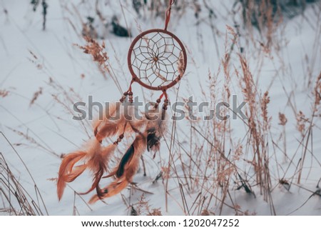 Dreamcatcher flying freely on snow background. Handmade decor with feathers and colorful beads.