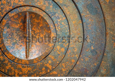Abstract metal background with geometric holes in a circle and rust texture orange-brown with spots. Selective focus