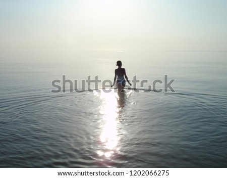    Photo of a girl from the back going into the sea against the background of quiet water merging with the sky on the horizon.                            
