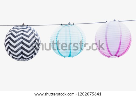 Three paper lanterns on a string - soft blue, pink and patterned black and white. High key photo. White background