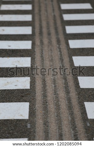 Close up view of pattern of white signs painted on an asphalt surface. Leading lines for pedestrians in a french parking. Geometric shapes to show the  pathway. Abstract image with graphic symbols.