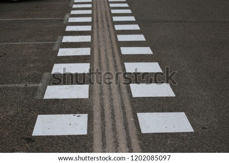 Close up view of pattern of white signs painted on an asphalt surface. Leading lines for pedestrians in a french parking. Geometric shapes to show the  pathway. Abstract image with graphic symbols.