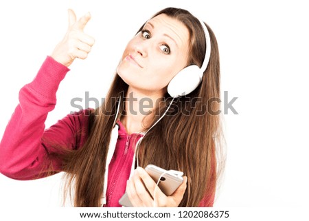 Young attractive smiling girl with long hair and pierced tongue listening the music by smartphone with headphones and making faces. Advertising concept isolated on abstract blurred white background