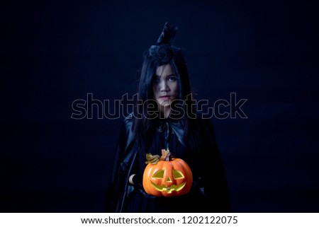 Studio shot young Asian woman costume in black witch on mesh hat with hand holding a orange halloween jack'o pumpkin on black backgroung, concept for halloween fashion festival.