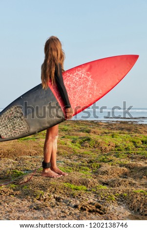 People, resort, recreation. Full length shot of brave girl ready to hit waves for first time, carries surfboard with fixed legrope serves as connection to board, has thoughtful look at peaceful ocean