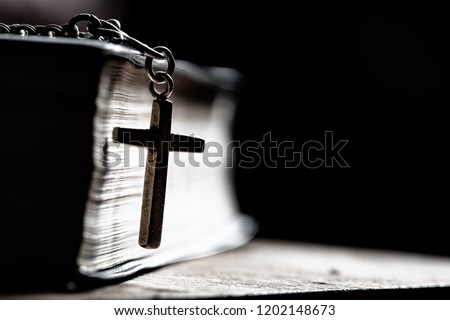 Cross with Bible on a old oak wooden table. Beautiful dark background. Religion concept
