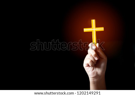 Human hand holding and lift of christian cross with light black background