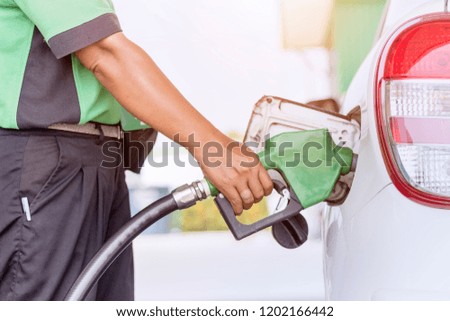Close up picture of hand is fueling a petroleum to white vehicle at gas station in warm sunlight.