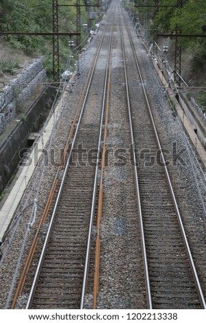 Outdoor view from above of straight railways with electric high iron poles and vegetation on each side. Symbol picture of transportation and travel with leading parallel lines. Empty long way.