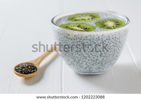 Glass bowl with milk Chia seed pudding and wooden spoon on white wooden table.