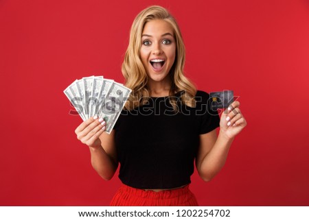 Image of young excited woman holding money and credit card isolated over red background.