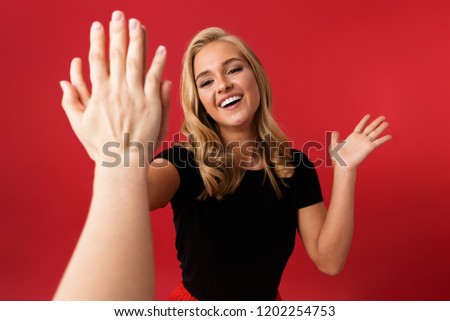 Image of young excited woman looking camera give a high five to someone's hand isolated over red background.