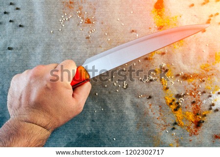 Flat lay. Close-up of a male chef hand holding a kitchen knife, the cook is preparing to cut food against the background of the kitchen table with sprinkled spices, salt, pepper, top view.