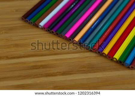 Multi-colored pencils lined up in a row and on brown background.