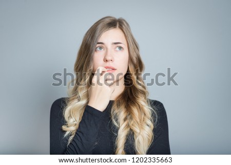 closeup blond woman worries and bites her nails, isolated over gray background