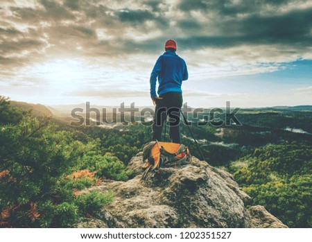 Tall photographer with baseball cap and tripod with camera in hands stand on rocky view point and watching down to deep misty valley bellow