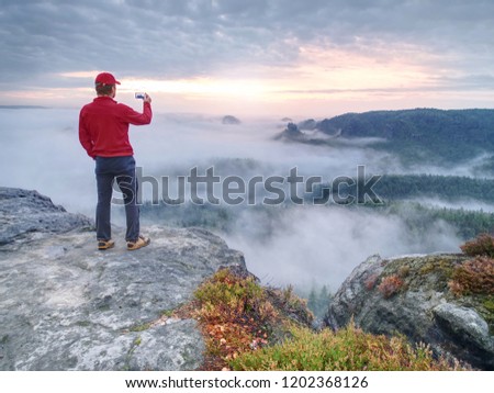 Tall man hiking in autumn nature. Bad Schandau range, Germany, 21st of August 2018.  Tourist on the mountain taking photos with touch screen smartphone