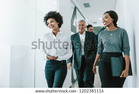 Diverse group of business people walking through office corridor.  Team of corporate professionals walking and talking in modern office hallway. Royalty-Free Stock Photo #1202381116