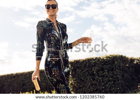 Stylish young woman walking with glass of wine. Wealthy female with wine walking outdoors. Royalty-Free Stock Photo #1202385760
