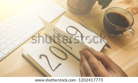 New Year 2019 is coming concept. Female hand flips notepad sheet on wooden table in sunlight. 2018 is turning, 2019 is opening, toned Royalty-Free Stock Photo #1202417773