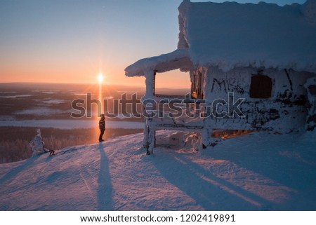 Sunset in Levi, Finland, frozen wooden house in Lapland, Santa's House made for movie, winter, person's silhouette 
