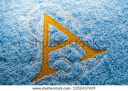 Embroidery yellow monogram alphabet design on blue towel, close up picture