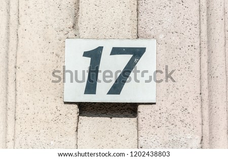 Old vintage house address metal plate number 17 seventeen on the plaster facade of abandoned home exterior wall on the street side