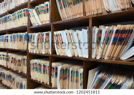 A wall with rows of wooden shelves filled with color-coded and numbered folders full of papers as medical documents from a clinic in horizontal format.