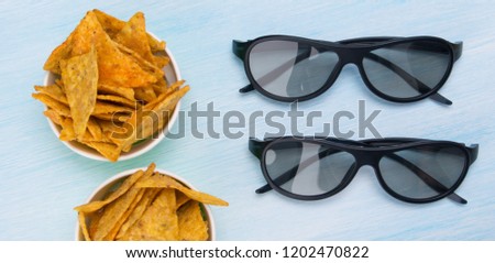 two pairs of 3D glasses on a blue table, next to the buckets of nachos