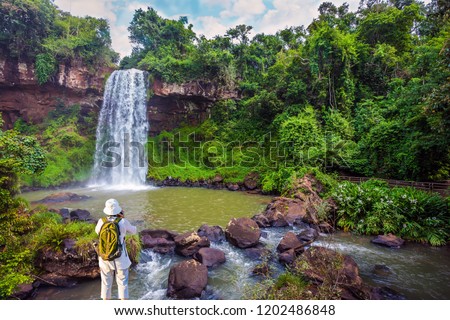 Scenic basaltic rock formations famous waterfalls Iguazu Falls. Energetic woman with a tourist backpack pictures a waterfall. Concept of active and phototourism