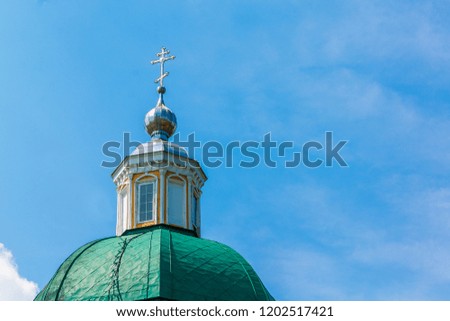Green dome of a Christian temple with a silver cross against the blue sky with white clouds. Image contains copy space.