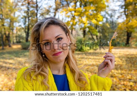 A young, beautiful, blonde woman walking through the autumn park and rejoice in colorful tree leaves.