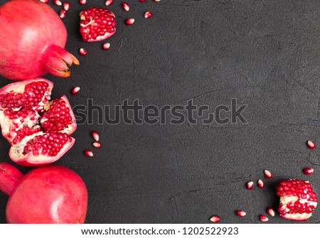 Ripe red pomegranate closeup photography on black background with copy space - top view on seasonal raw whole and cut juicy fruit with seeds in dark mood style with empty space for text.