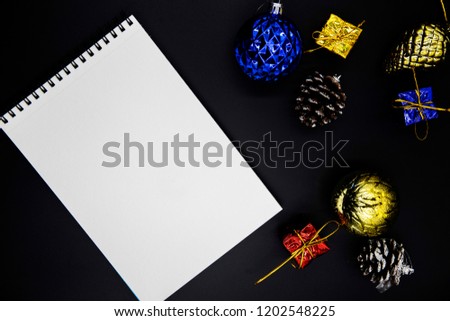 Christmas decor and white paper notebook flat lay on black background. Christmas or New Year mockup. Drawing pad with spiral and blank page. Blue and golden Christmas tree toys. Winter holiday banner