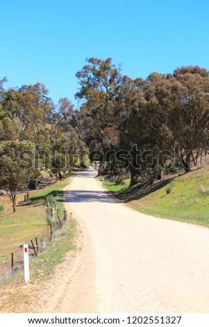 Countryside winding curvy dirt bitumen road in the south Australian idyllic pastoral near Melrose and Flinders Ranges. Fence, green grass and tree lined with clear blue sky horizon.