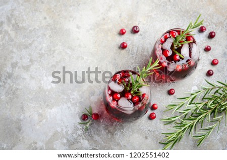Cold refreshing drink with cranberries and rosemary on a gray concrete background.
