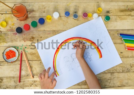 Children's hands paint a drawing with a brush and paints. Top view
