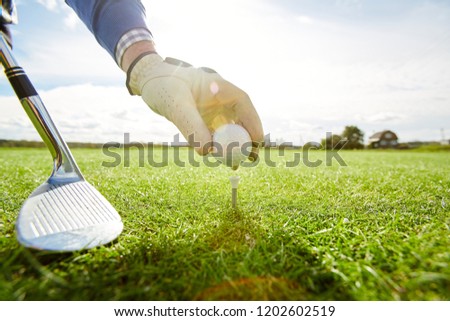 Golf player with club putting ball on tee before start of game on green play field