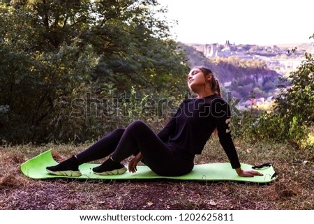 Beautiful blonde caucasian girl in green swimsuit doing asana balancing on her shoulders with twisted legs in the air on a sunny summer day in park. Yoga concept. Healthy lifestyle concept.