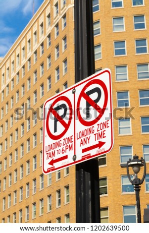 "No Parking Loading Zone" sign with downtown buildings in background.