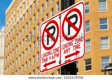 "No Parking Loading Zone" sign with downtown buildings in background.