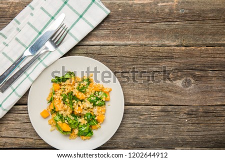 Plate with bulgur and pumpkin with spinach on old worn background