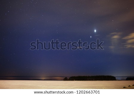 Conjuction of planets Jupiter and Venus on night sky above frozen lake.