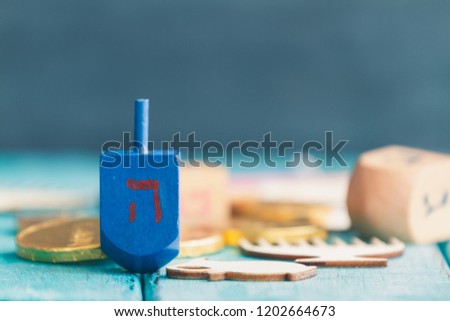 Hanukkah dreidels with some Hanukkah coins and Hanukkah candles on a vintage wood green background. Translation of the hebrew text: Letter H

