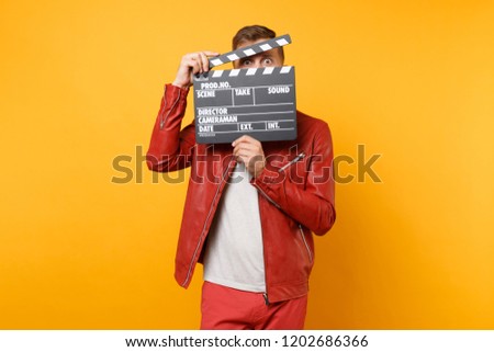 Portrait vogue smiling young man in leather jacket, t-shirt holding classic black film making clapperboard isolated on bright trending yellow background. People lifestyle concept. Advertising area Royalty-Free Stock Photo #1202686366