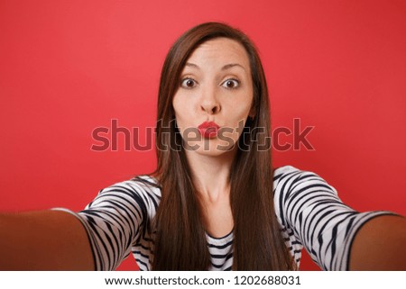 Close up selfie shot of funny young woman in casual striped clothes blowing kisses send air kiss isolated on bright red wall background. People sincere emotions, lifestyle concept. Mock up copy space