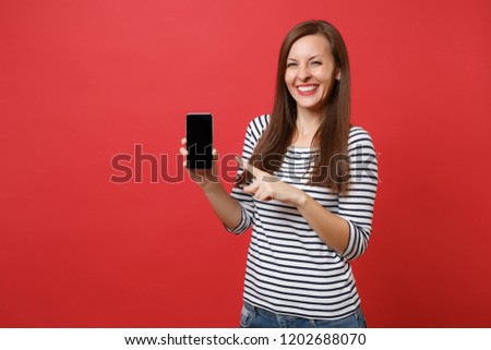 Portrait of pretty young woman pointing index finger on mobile phone with blank black empty screen isolated on bright red background. People sincere emotions, lifestyle concept. Mock up copy space