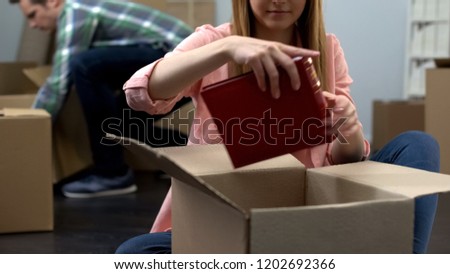 Young woman unpacking photo album from box, couple moving to new apartment