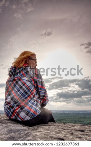 Young woman in striped jacket take a rest on rocky summit above forest valley. Spring sunny weather with warm colors. 